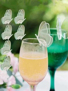 a wine glass filled with liquid next to a vase full of flowers and butterfly decorations