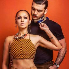 a man and woman standing next to each other in front of an orange wall wearing jewelry