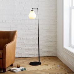 a lamp on the floor next to a chair in a room with white brick walls