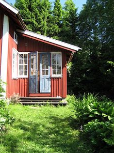 a small red house sitting in the middle of a lush green field next to trees