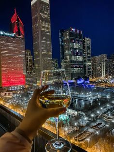 a person holding up a wine glass in front of a cityscape at night