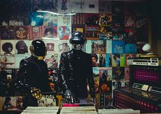 two mannequins wearing helmets in front of a wall covered with posters and records