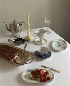 a table topped with plates and bowls filled with cake next to silver ware on top of a white table cloth