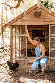 a woman kneeling down in front of a chicken coop with her arm up on the door