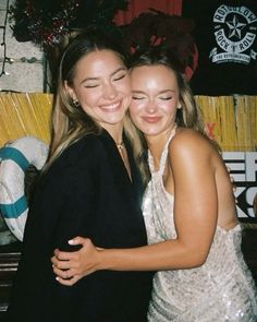 two young women hugging each other in front of a christmas tree