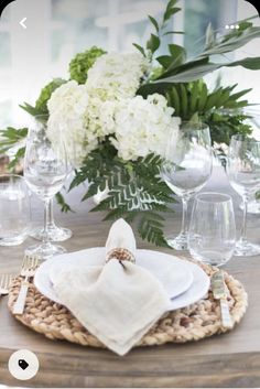 a place setting with white flowers and greenery in the center, on a wooden table