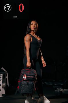 a woman is holding a black bag and posing for the camera in front of a dark background