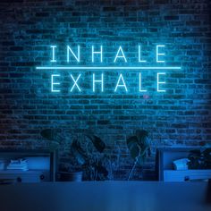 a neon sign that reads inhale exhale on a brick wall above a desk