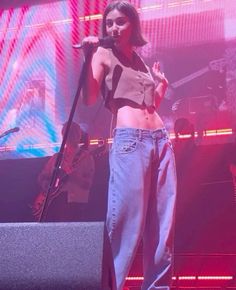 a woman standing on top of a stage with a microphone in her hand and wearing high waist jeans