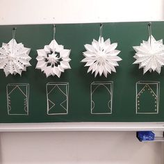 five paper snowflakes hanging from hooks on a green board