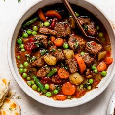 a white bowl filled with meat and veggies next to crackers on the side