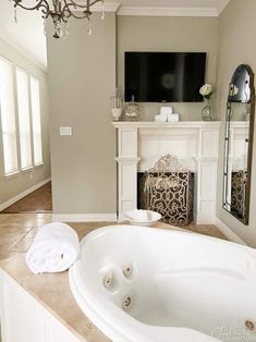 a large white bath tub sitting in a bathroom next to a fireplace with a tv on top of it