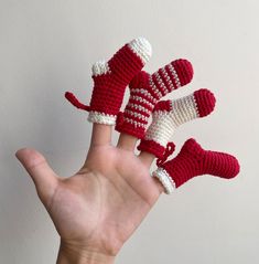 a hand is holding four crocheted red and white mittens in the air