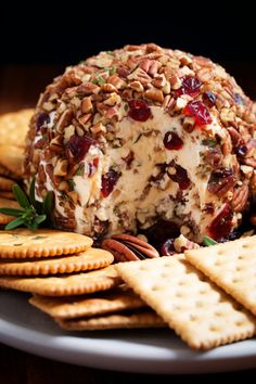 a cheese ball covered in nuts and cranberries on a plate with crackers