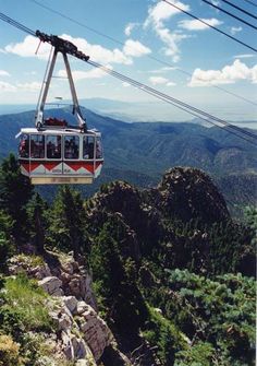 a gondola with people riding on it above the mountains and trees in the foreground