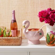 a swan shaped teapot with pink flowers in it next to bottles of wine and glasses