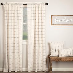 a window with white curtains and pillows next to a wooden bench in front of it