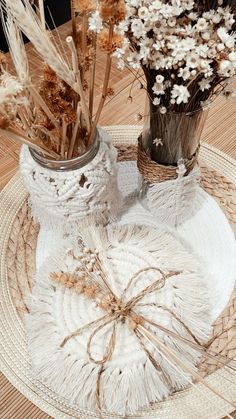 two vases filled with dried flowers sitting on top of a white doily plate