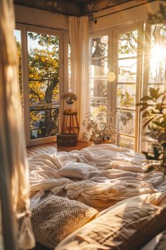 an unmade bed with white sheets and pillows in front of large windows overlooking trees