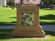 the memorial park sign is in front of some green grass and trees with pink flowers