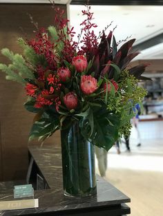 a vase filled with red flowers on top of a wooden table next to a sign