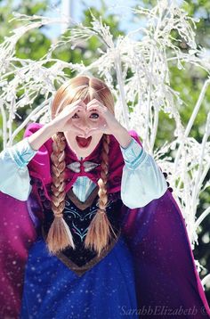 a woman dressed as disney frozen princess holding her hands up to her face while standing in front of trees