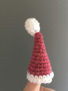 a hand is holding a small knitted santa's hat with white and red trim