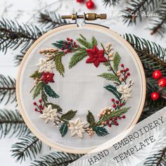 an embroidered christmas wreath with poinsettis and holly on white fabric surrounded by pine needles