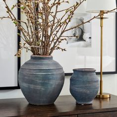 two vases sitting on top of a wooden table next to a lamp and pictures