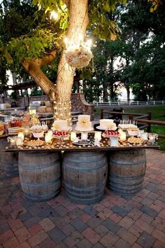 a table topped with cakes and desserts on top of wooden barrel tables next to trees