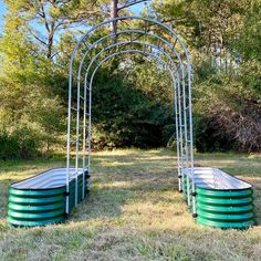 two green barrels sitting in the middle of a field next to an arch made out of metal pipes