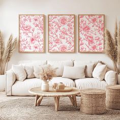 a living room with white furniture and pink paintings on the wall above it's couches