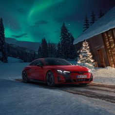 a red car driving down a snow covered road next to a cabin under the aurora lights