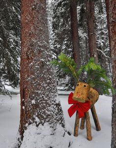 a wooden reindeer with a red bow standing in the snow next to some tall trees