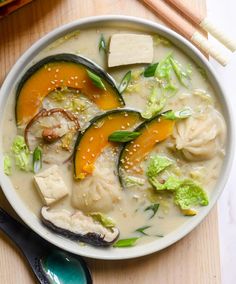 a bowl filled with soup and vegetables on top of a wooden table next to chopsticks