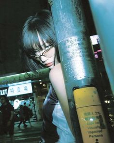 a woman leaning on a pole with her head against the pole and looking at the camera