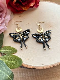 a pair of black and gold dragonfly earrings sitting on top of a piece of wood