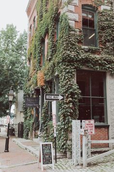 an old brick building with ivy growing on it's side and street signs in front