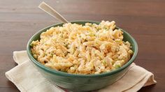 a green bowl filled with rice and vegetables on top of a wooden table next to a napkin