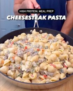 a skillet filled with cheesesteak pasta on top of a wooden table next to a person