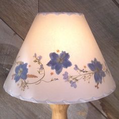 a lamp with blue flowers painted on it sitting on a wooden table next to a wall