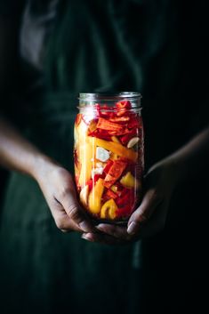 a person holding a jar filled with sliced fruit in it's hands and wearing an apron