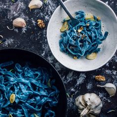 two bowls filled with blue pasta next to garlic and cloves on a table