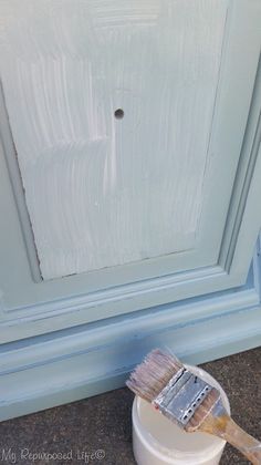 a paint can and brush sitting on the ground next to a painted cabinet door with chipped paint