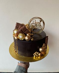 a chocolate cake with gold decorations on top is being held by someone's hand