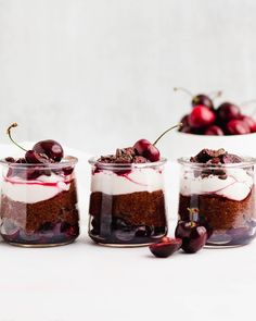 three small jars filled with dessert and cherries