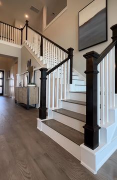 a white staircase with black railing and wooden handrails in a large home's entryway