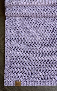 a purple crocheted blanket sitting on top of a wooden table next to a cup