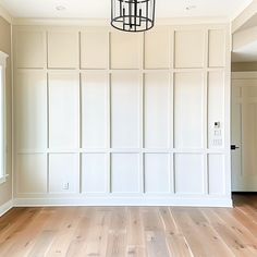 an empty room with white paneling and wood floors in the center is a chandelier