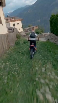 a person riding a motorcycle down a lush green hillside next to a building with mountains in the background